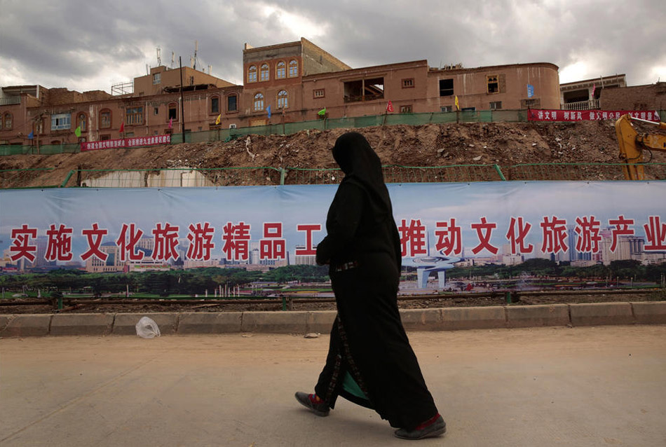 يتم تنفيذ إعادة إعمار الكثير من المساكن القديمة في كاشي، وتظهر الصورة أن إمرأة من قومية الويغور تمر بموقع البناء. 