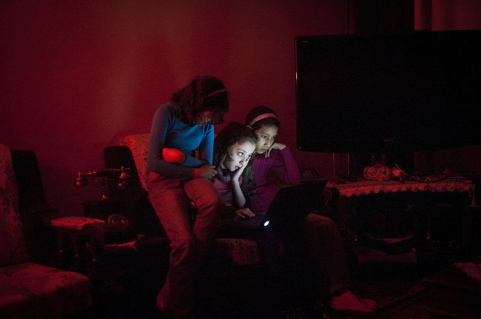 فتيات يشاهدن جهاز الكمبيوتر في وقت انقطاع التيار الكهربائي. نقص الوقود في غزة، لذلك، يتم توفير الكهرباء للعديد من الأسر 6-8 ساعات كل يوم. 