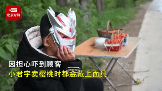 طفل يرتدي قناع ألترامان لتغطية ندوب وجهه أثناء بيع الكرز