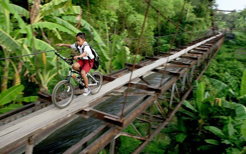 تلميذ يعبر الجسر المعلق الخطير في جزيرة جاوة باندونيسيا. وتحت الجسر المعلق خندق، وعلى الجسر طريق خشبي ضيق فقط يسمح لحركة دراجة واحدة.  ولكن، هذا الجسر المعلق هو طريق مختصر يمكنه توفير الكثير من الأوقات. تتجاوز الرحلة إلى المدرسة 6 كيلومترات في حالة عدم عبور الطريق المختصر الخطير. 