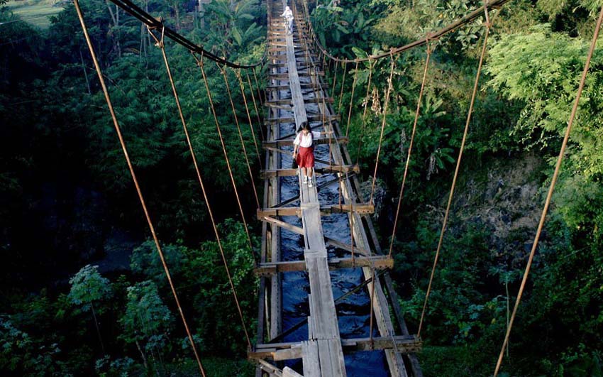 فتاة تعبر الجسر المعلق الخطير في جزيرة جاوة باندونيسيا.