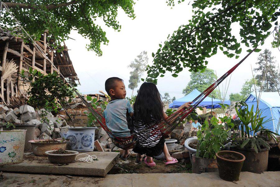 طفلان يلعبان أمام منزل دمره الزلزال بقرية تشينغلونغ في محافظة لوشان التابعة لمدينة ياآن بمقاطعة سيتشوان في 26 إبريل الجاري.
